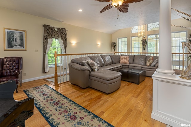 living room with lofted ceiling, ceiling fan with notable chandelier, ornate columns, and light wood-type flooring