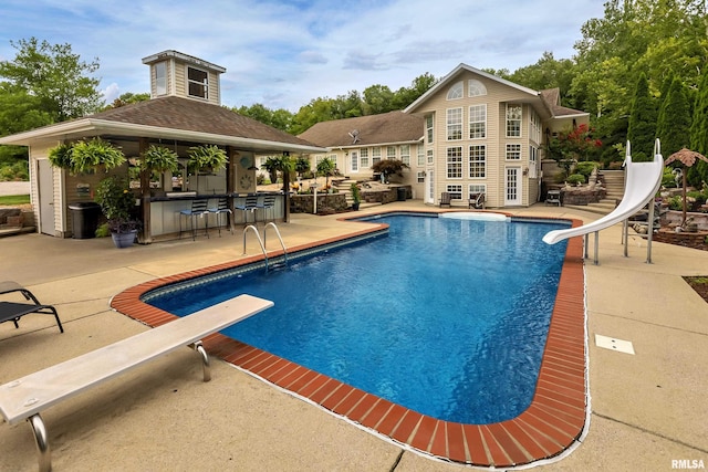 view of pool with a bar, a patio, a diving board, and a water slide