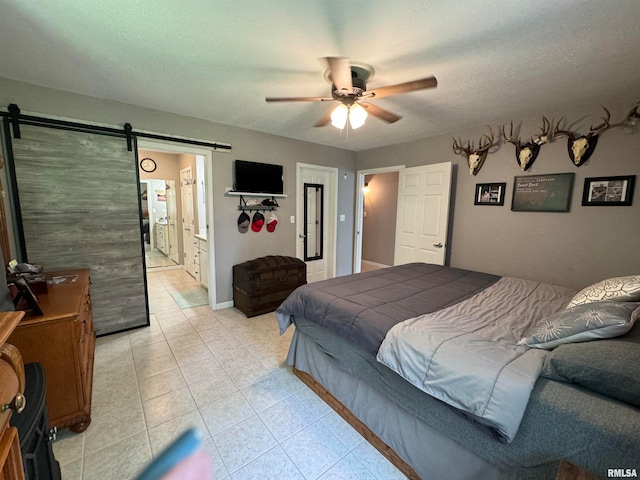 bedroom featuring light tile patterned flooring, a textured ceiling, a barn door, ceiling fan, and ensuite bath