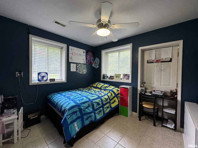 bedroom with a textured ceiling, multiple windows, light tile patterned floors, and ceiling fan