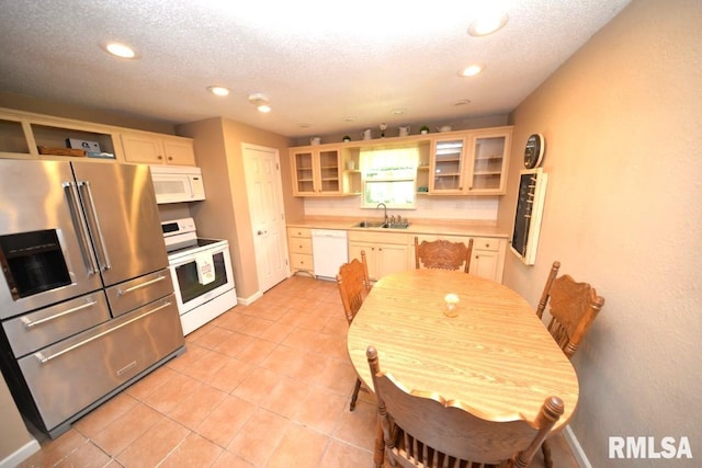 kitchen with a textured ceiling, sink, light tile patterned flooring, and white appliances