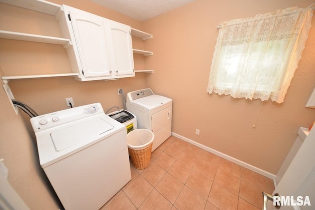 clothes washing area with washer and clothes dryer, light tile patterned flooring, and cabinets