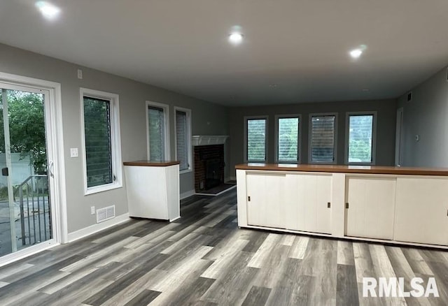 kitchen with white cabinetry, a brick fireplace, a wealth of natural light, and wood-type flooring