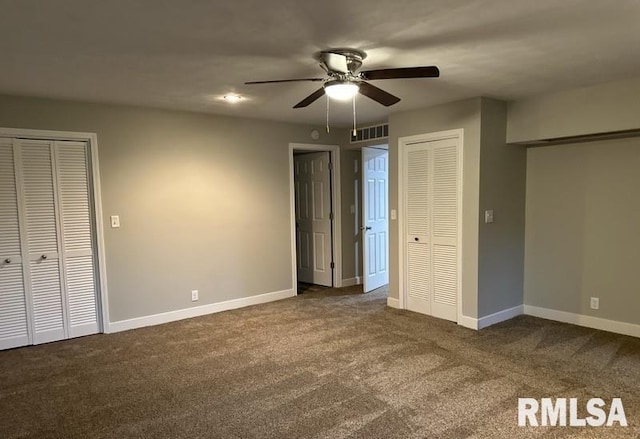 unfurnished bedroom with dark carpet, ceiling fan, and two closets