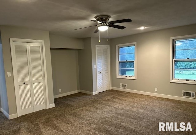 unfurnished bedroom featuring multiple closets, ceiling fan, and dark colored carpet