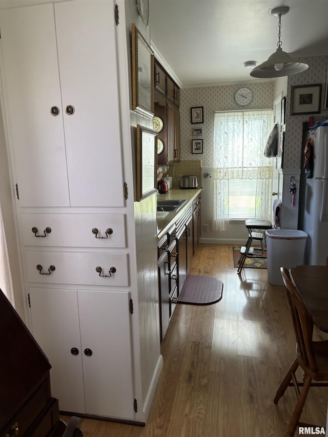 kitchen with white fridge, pendant lighting, white cabinets, and light hardwood / wood-style flooring