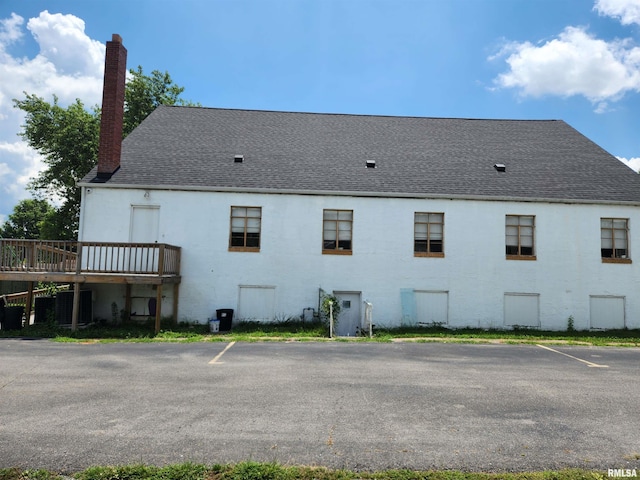 back of house featuring a wooden deck, roof with shingles, uncovered parking, and a chimney