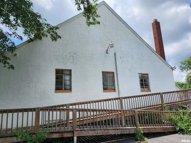 view of property exterior with a deck, a chimney, and stucco siding
