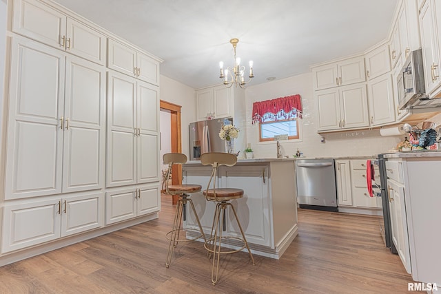 kitchen with appliances with stainless steel finishes, white cabinets, a breakfast bar, light hardwood / wood-style floors, and an inviting chandelier