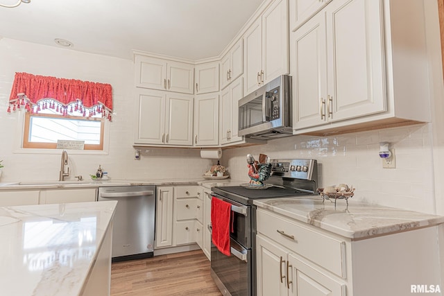 kitchen featuring tasteful backsplash, stainless steel appliances, light hardwood / wood-style floors, light stone countertops, and sink