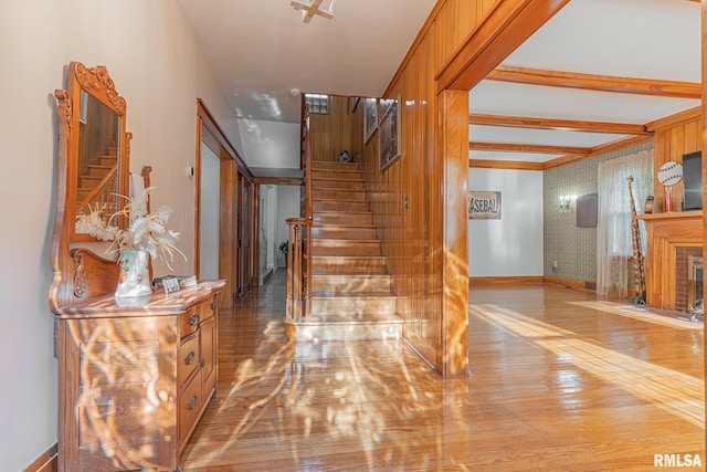 staircase featuring beamed ceiling, wood-type flooring, and a brick fireplace