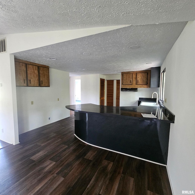 kitchen with dark wood-type flooring, kitchen peninsula, a textured ceiling, and sink