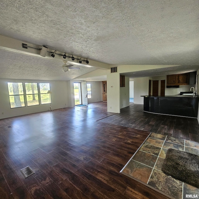 unfurnished living room with track lighting, a textured ceiling, sink, dark hardwood / wood-style floors, and vaulted ceiling