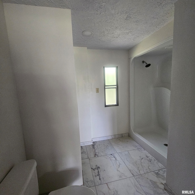 bathroom with a textured ceiling, toilet, and walk in shower