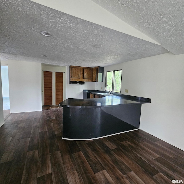 kitchen with a textured ceiling, dark wood-type flooring, kitchen peninsula, and sink