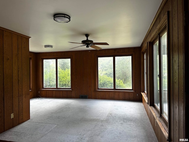 carpeted spare room with ceiling fan, wooden walls, and a healthy amount of sunlight