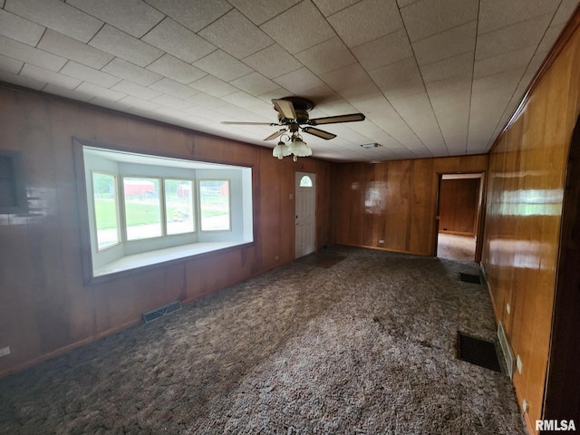 carpeted empty room featuring wood walls and ceiling fan