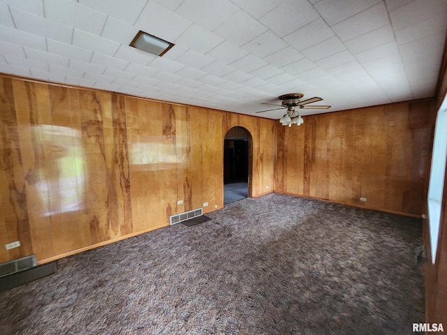 spare room featuring dark carpet, wood walls, and ceiling fan