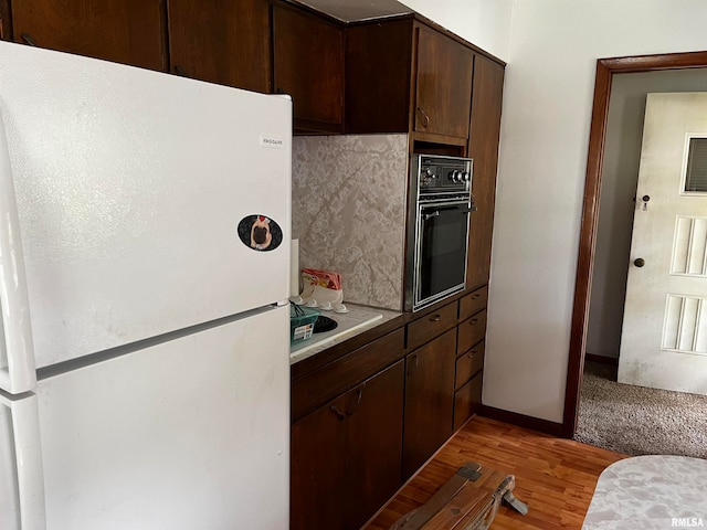 kitchen featuring light hardwood / wood-style floors, decorative backsplash, oven, dark brown cabinets, and white refrigerator