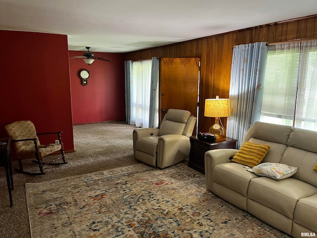 living room with wood walls, ceiling fan, and carpet