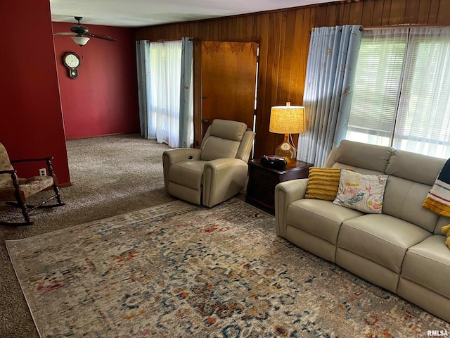 living room with wood walls, a wealth of natural light, carpet, and ceiling fan