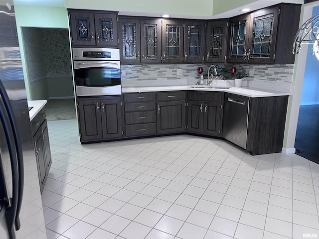 kitchen featuring stainless steel appliances, light countertops, decorative backsplash, glass insert cabinets, and a sink