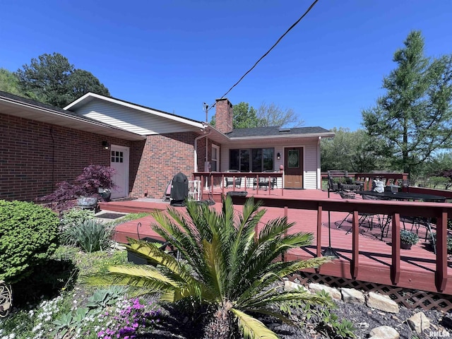 back of property with a deck, brick siding, and a chimney