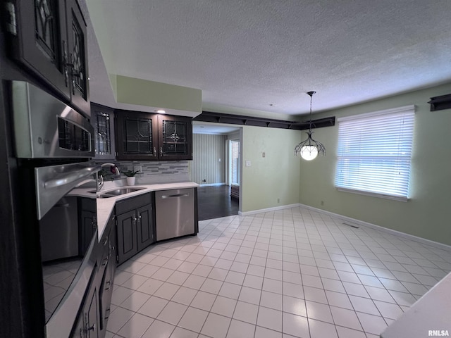 kitchen featuring light countertops, stainless steel dishwasher, dark cabinetry, and tasteful backsplash