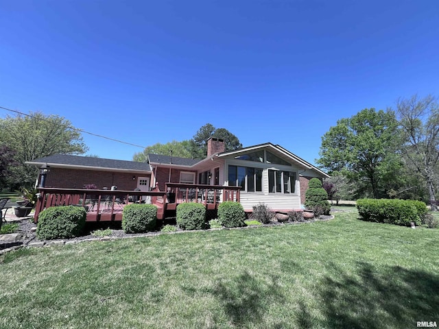 rear view of house featuring a yard, brick siding, a chimney, and a wooden deck