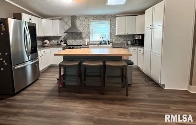 kitchen featuring white cabinetry, wall chimney range hood, dark hardwood / wood-style flooring, stainless steel fridge with ice dispenser, and a kitchen island