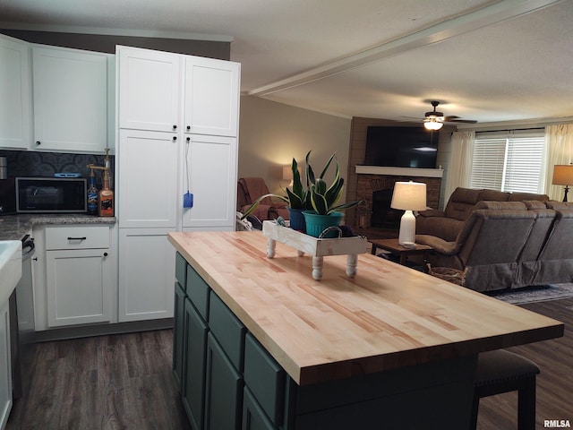 kitchen with butcher block counters, white cabinets, dark wood-type flooring, ceiling fan, and a brick fireplace