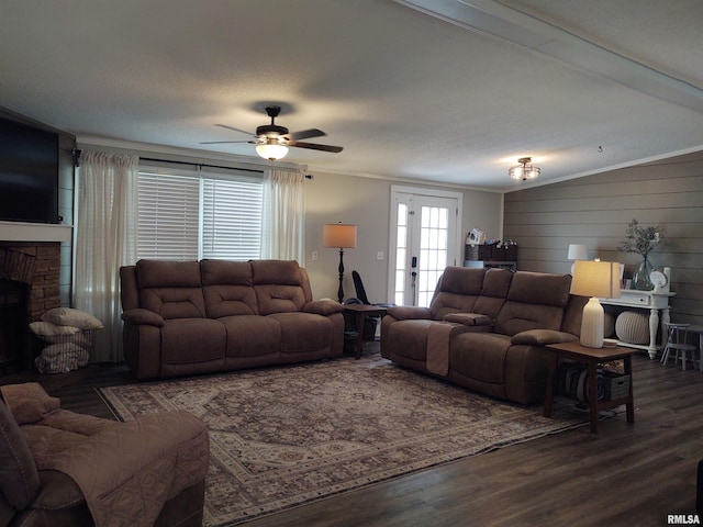 living room featuring ceiling fan, a stone fireplace, dark hardwood / wood-style flooring, ornamental molding, and a textured ceiling