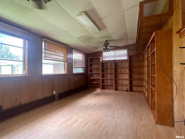 empty room with wood walls, a paneled ceiling, built in features, light wood-type flooring, and ceiling fan