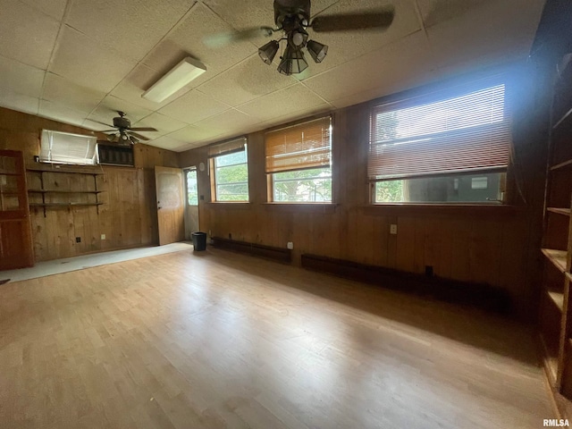 spare room with ceiling fan, wooden walls, hardwood / wood-style floors, and a drop ceiling