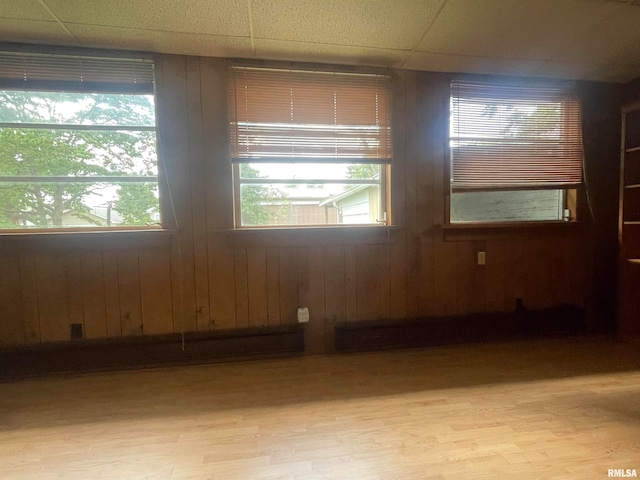 unfurnished room with a paneled ceiling, light hardwood / wood-style floors, and wooden walls