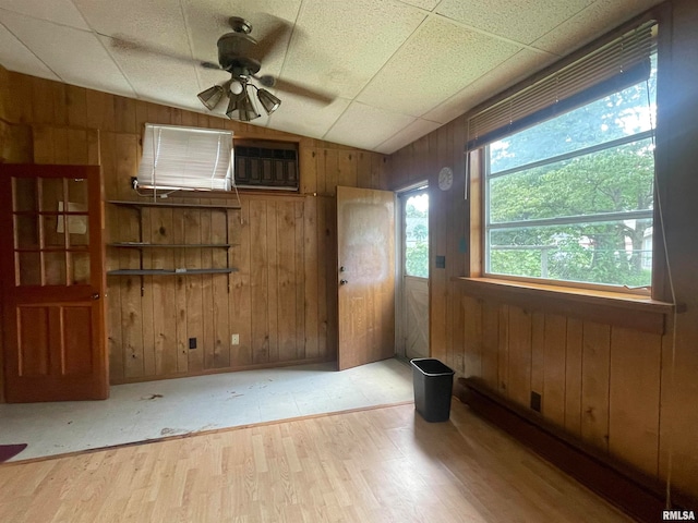 unfurnished room with a drop ceiling, wooden walls, ceiling fan, and light wood-type flooring