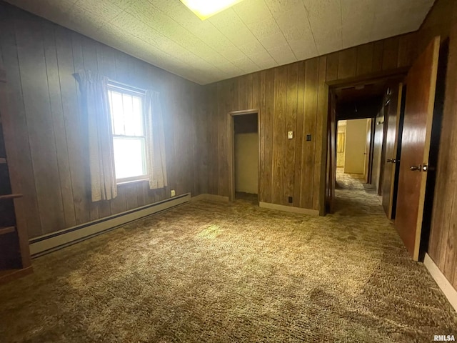 carpeted empty room featuring wooden walls and baseboard heating