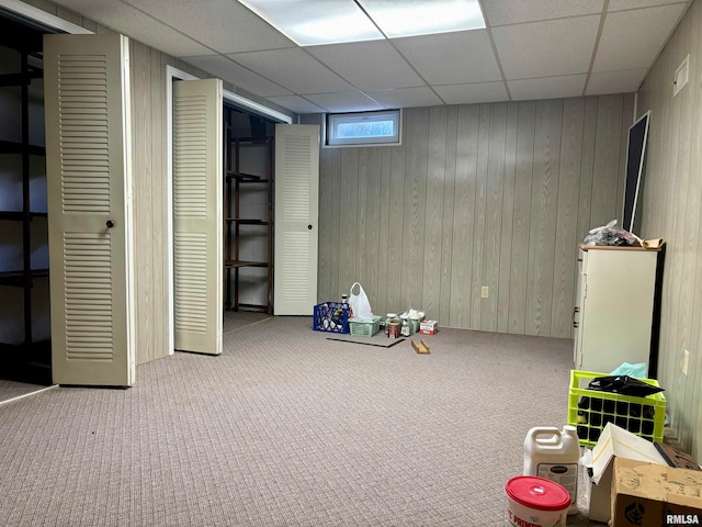 recreation room with a drop ceiling, carpet, and wood walls