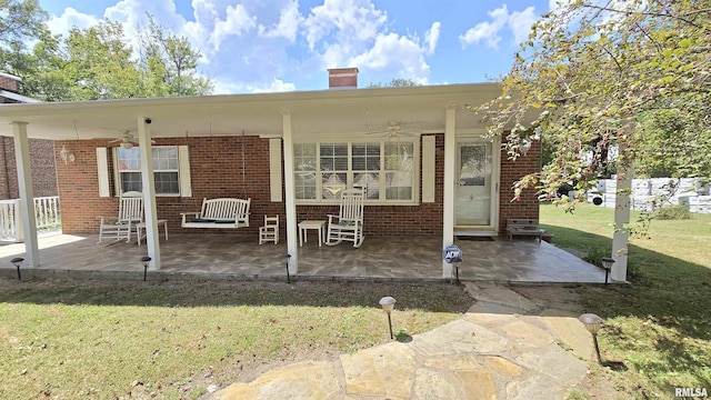 back of house featuring a yard, a chimney, a ceiling fan, and brick siding