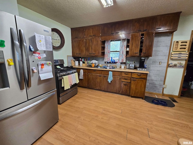 kitchen with appliances with stainless steel finishes, decorative backsplash, a textured ceiling, and light hardwood / wood-style flooring