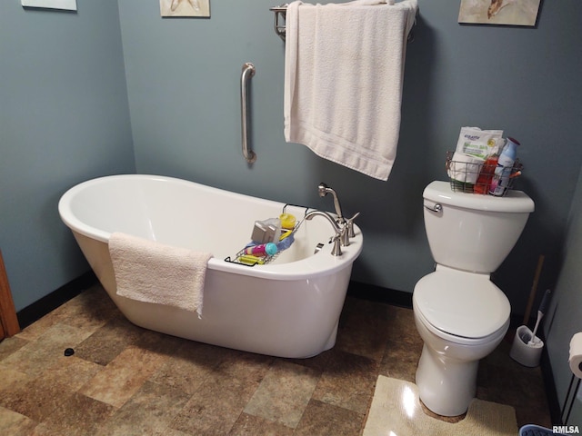 full bathroom featuring stone finish flooring, baseboards, a freestanding bath, and toilet