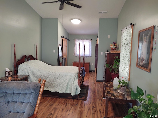 bedroom with a barn door, hardwood / wood-style floors, and ceiling fan