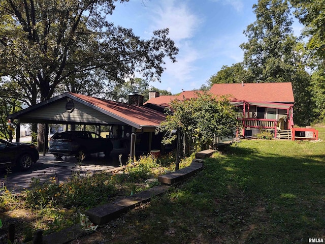 exterior space featuring driveway, a lawn, a chimney, a deck, and a detached carport