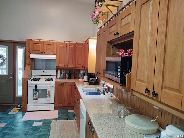 kitchen featuring white appliances, brown cabinetry, a towering ceiling, under cabinet range hood, and a sink