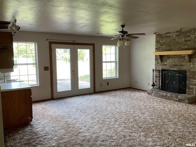 unfurnished living room with ceiling fan, carpet floors, a brick fireplace, and a healthy amount of sunlight