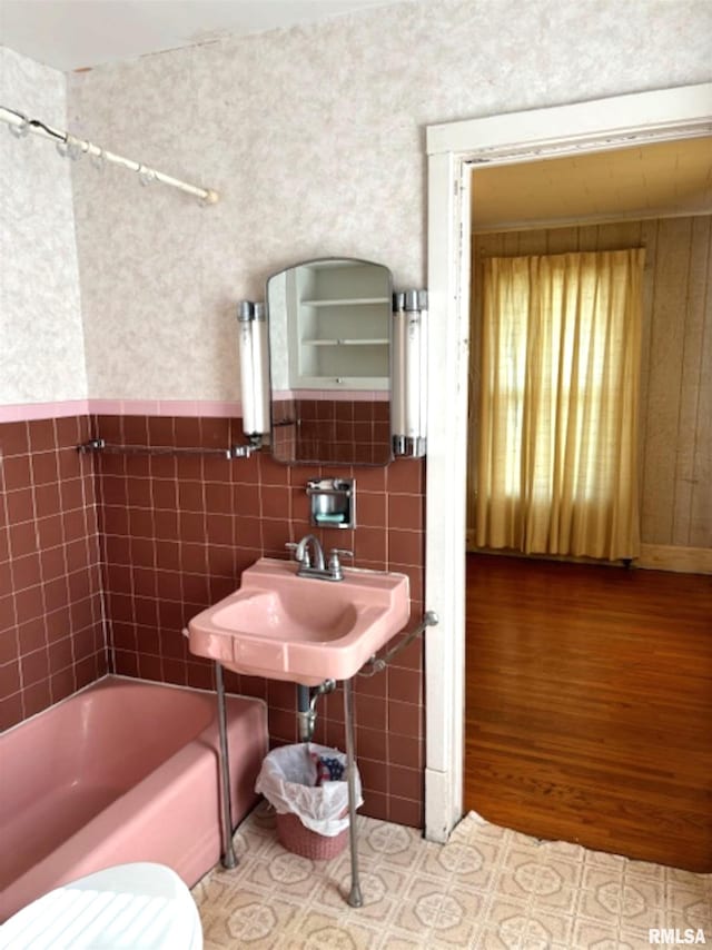 bathroom with toilet, hardwood / wood-style flooring, tiled shower / bath combo, and tile walls