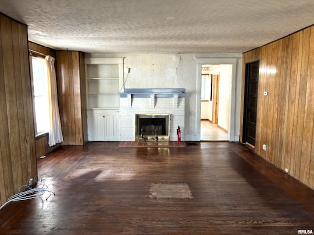 unfurnished living room featuring dark wood-type flooring, wood walls, a textured ceiling, and a brick fireplace