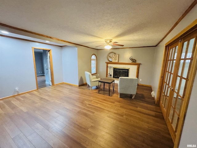 unfurnished room featuring ceiling fan, wood-type flooring, a textured ceiling, a fireplace, and ornamental molding