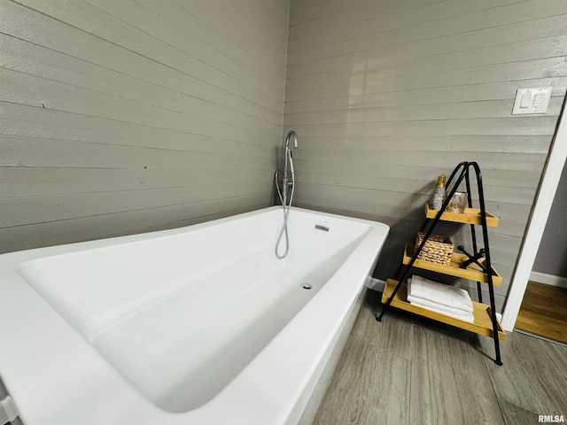 bathroom with wood-type flooring, a tub, and wooden walls