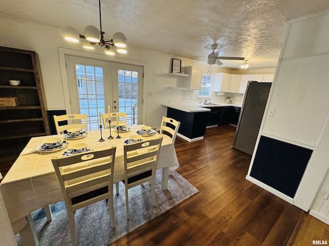 dining space with dark wood-type flooring, french doors, ceiling fan with notable chandelier, sink, and a textured ceiling